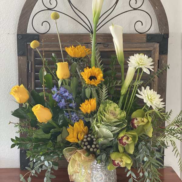 Mixed floral arrangement with yellow roses, white calla lilies, and sunflowers in a silver vase