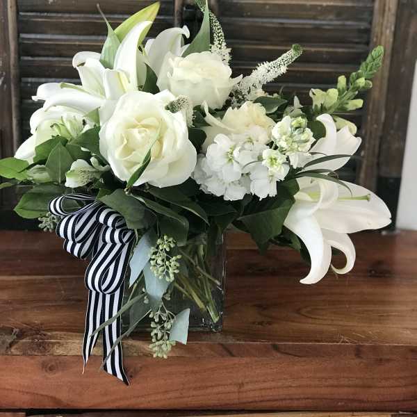 White lilies and roses in a glass vase with a striped ribbon