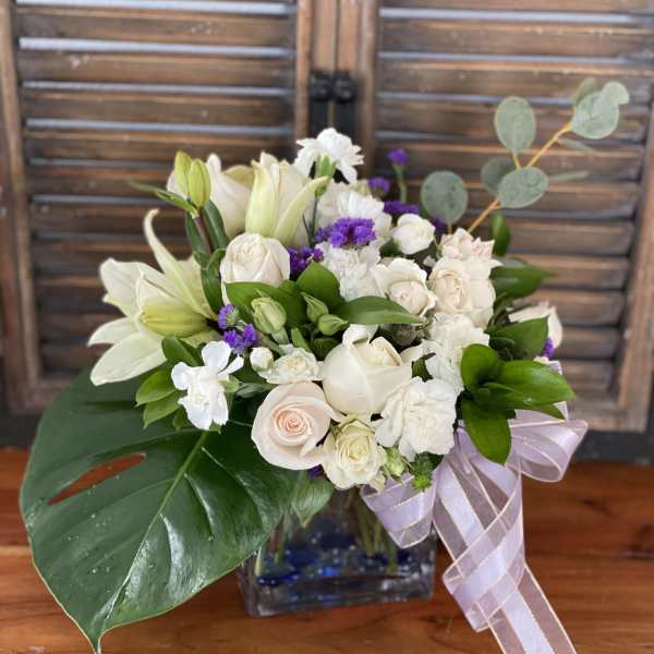 White roses and lilies in a glass vase with a lavender ribbon