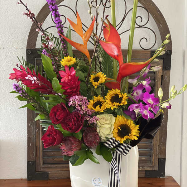 Colorful tropical flower arrangement in a white vase with a striped ribbon