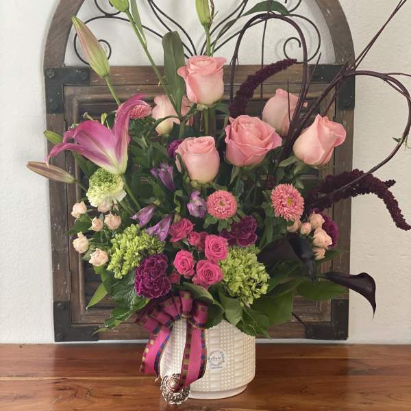 Pink roses and lilies arranged in a white vase with ribbon