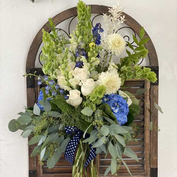 Tall bouquet of white, blue, and green flowers in a glass vase