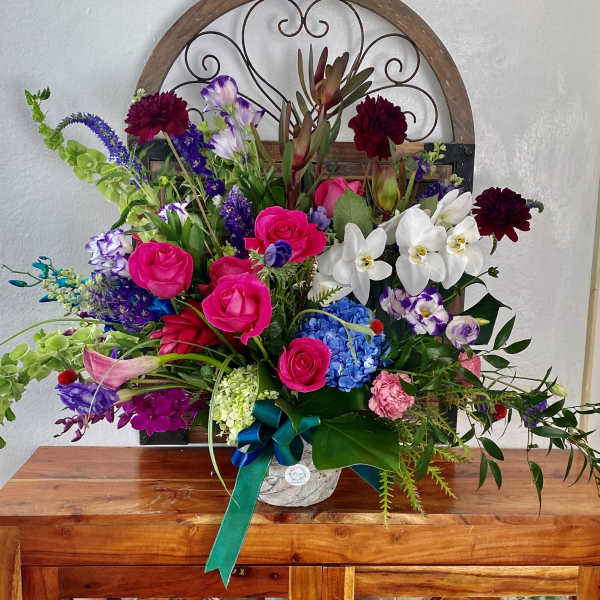 Colorful mixed flower arrangement in a white container with a teal ribbon