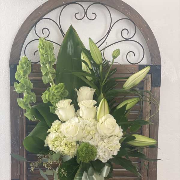 White roses and lilies arranged in a green vase with a ribbon