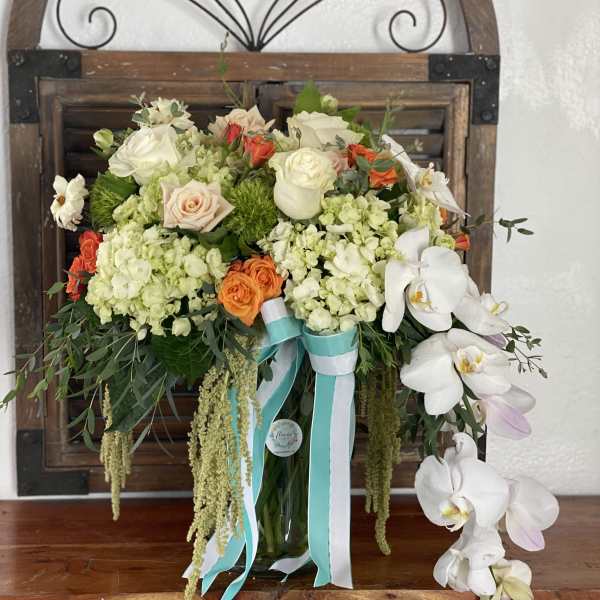 Bouquet of white orchids, roses, and hydrangeas in a glass vase with ribbons