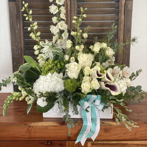 White floral arrangement in a white box with a teal ribbon