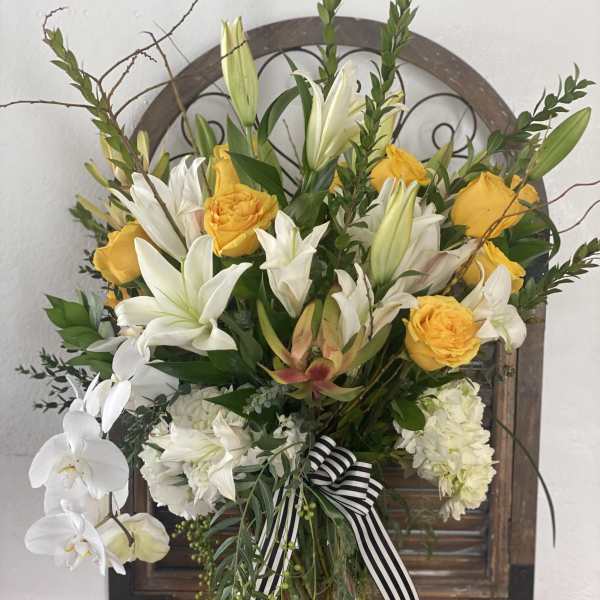 Yellow roses and white lilies in a glass vase with a striped ribbon