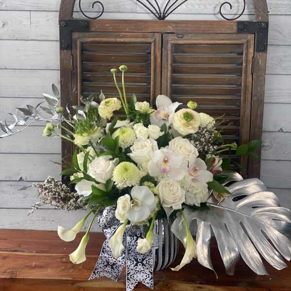 White and pale green floral arrangement in a striped vase with silver leaves