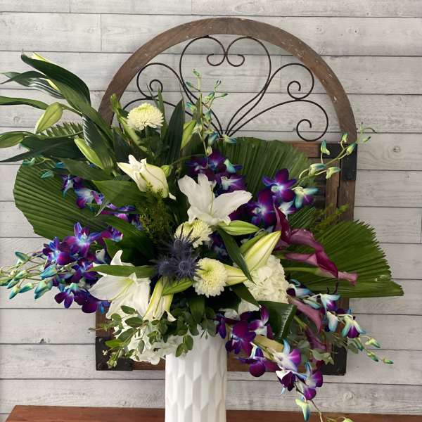 White lilies and purple orchids in a tall white vase