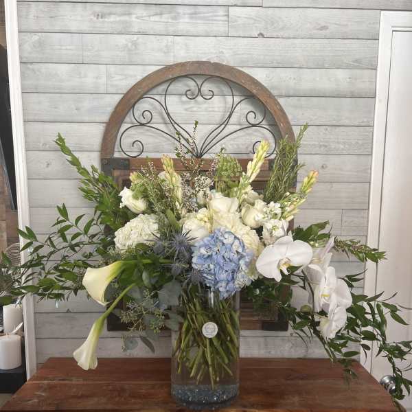 Large white and blue floral arrangement in a glass vase