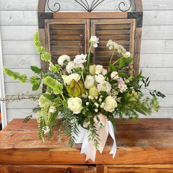 White and green floral arrangement in a white container with ribbon