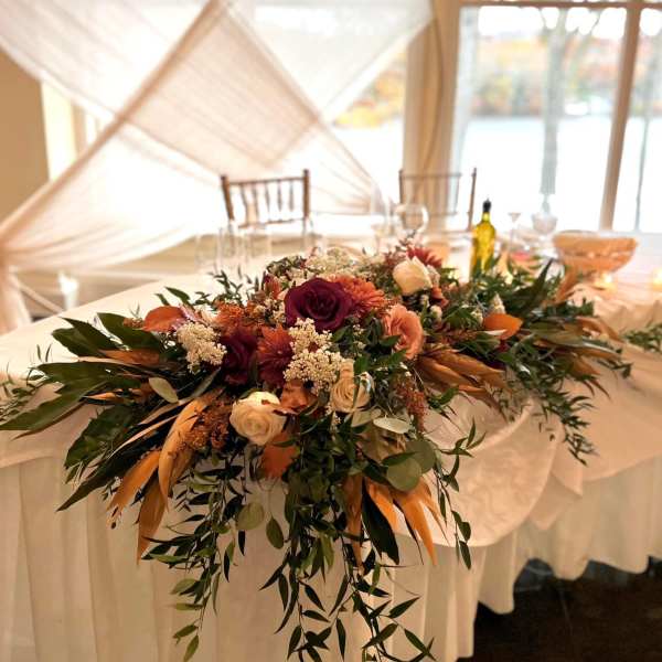 Low floral centerpiece with burgundy, peach, and cream blooms on a draped table