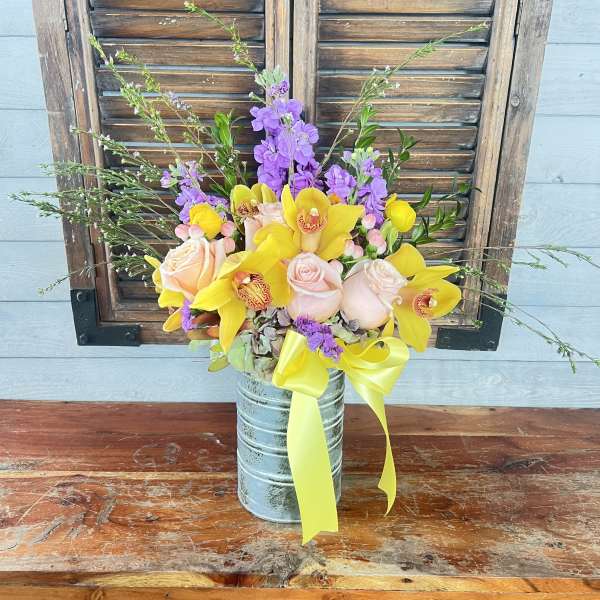 Yellow orchids and pale pink roses in a metal vase with a ribbon