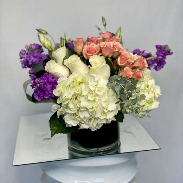 Mixed bouquet of roses, hydrangeas, and purple blooms in a glass vase