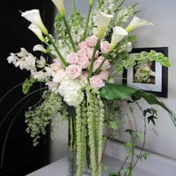 Tall arrangement of white calla lilies and pale pink roses in a vase