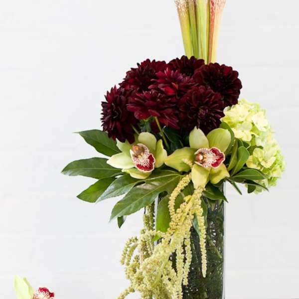 Tall floral arrangement with burgundy blooms, pale orchids, and a clear vase