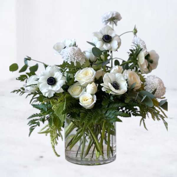 White anemones and roses arranged in a clear glass vase with lush greenery