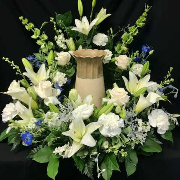 White lilies and roses arranged around a tall urn centerpiece