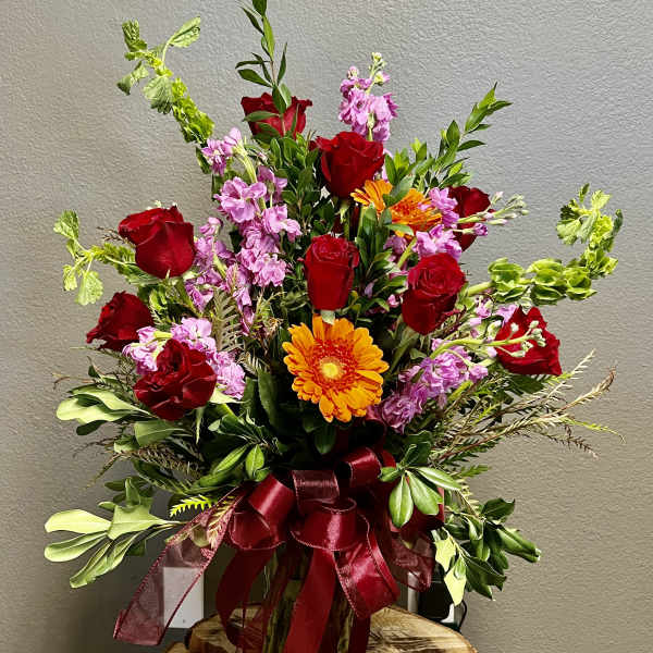 Bouquet of red roses, pink flowers, and orange gerbera daisies with a burgundy ribbon