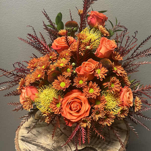 Orange roses and chrysanthemums in a low arrangement with burgundy foliage