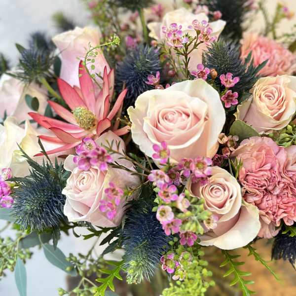 Bouquet of pale pink roses and pink blooms with blue thistle in a vase