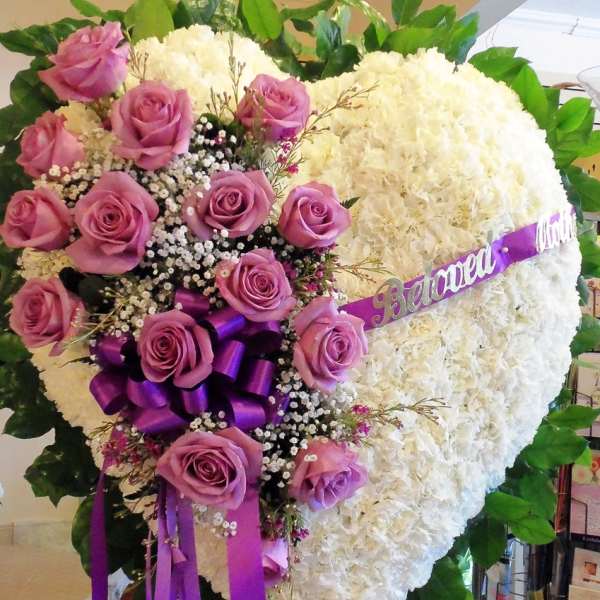 Heart-shaped floral tribute with pink roses and white blooms