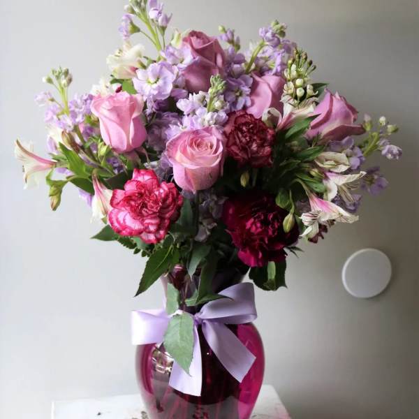 Pink and purple bouquet in a magenta glass vase with a lavender ribbon