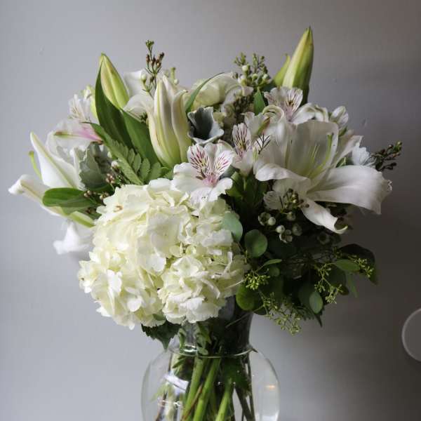 White floral bouquet in a clear glass vase with lilies and hydrangea