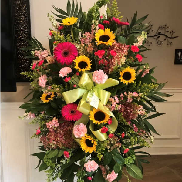 Standing floral spray with sunflowers, pink gerberas, and carnations on an easel
