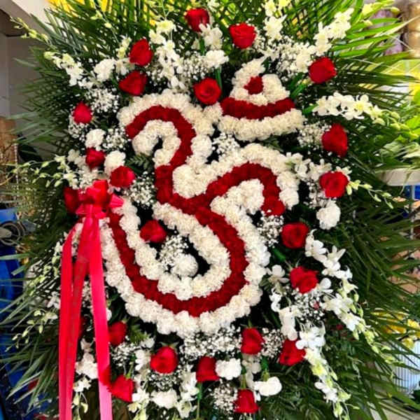 Large standing floral wreath with red and white flowers and a pink ribbon