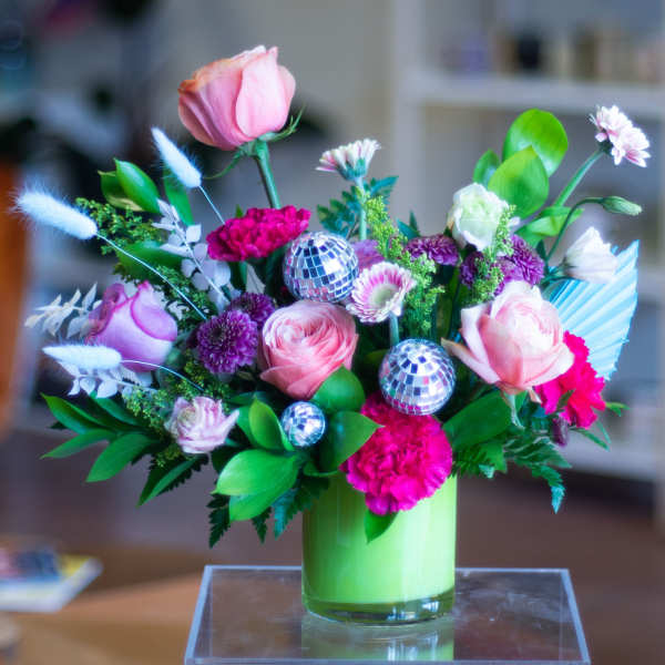 Pink and purple floral arrangement in a green vase with disco balls