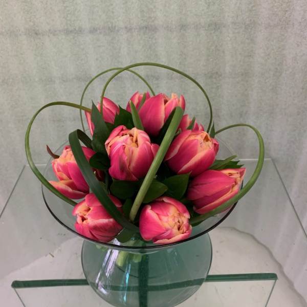 Pink tulips arranged in a clear glass vase with looping grass accents