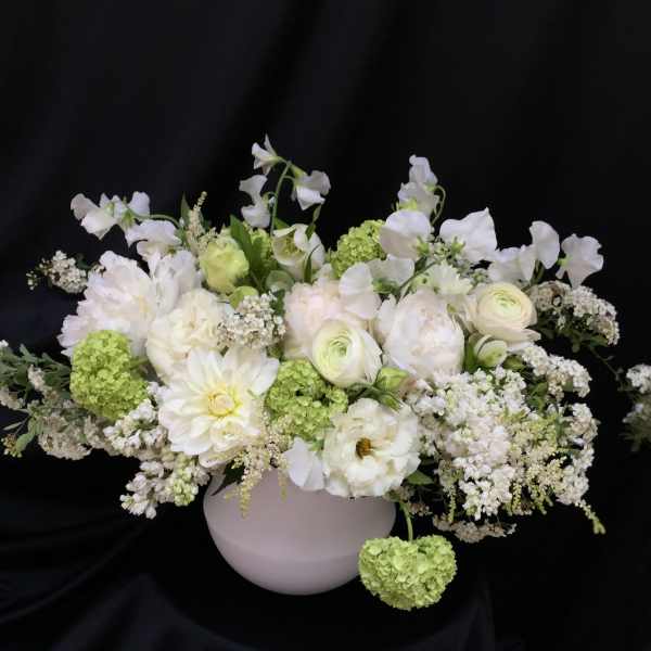 White floral arrangement in a round vase with green accents