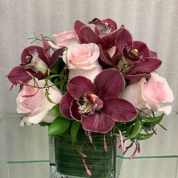 Pink roses and burgundy orchids in a square glass vase