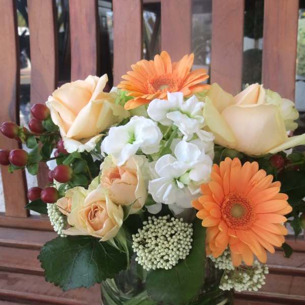 Bouquet of peach roses, orange gerbera daisies, and white flowers in a glass vase