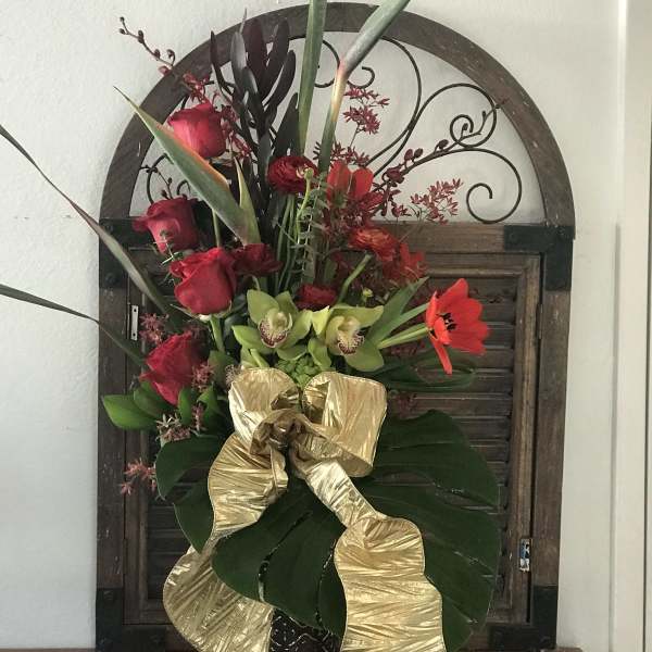 Tall tropical bouquet with red roses, green orchids, and a gold ribbon in a vase