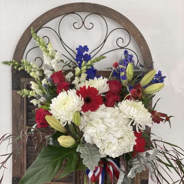 Mixed bouquet of red roses, white chrysanthemums, and blue flowers in a glass vase