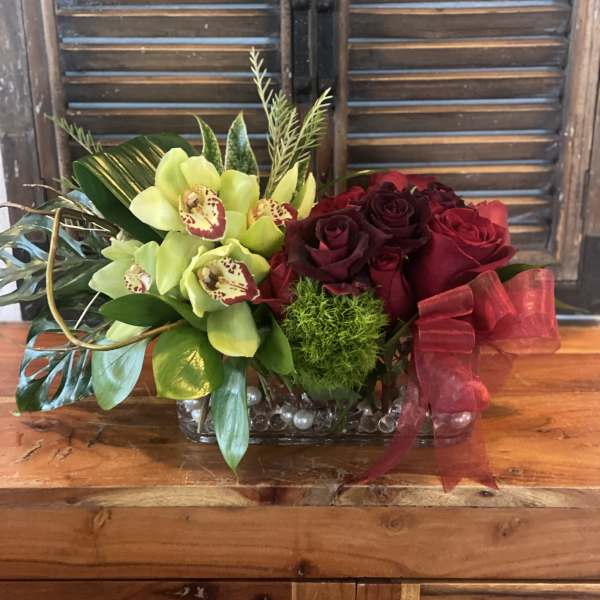 Red roses and green orchids in a glass vase with a red ribbon