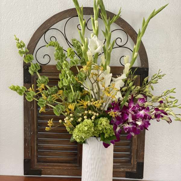 Tall floral arrangement in a white vase with white, green, yellow, and purple blooms