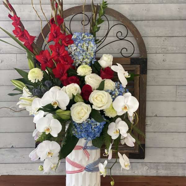 Tall floral arrangement with red gladiolus, white orchids, and blue hydrangeas in a white vase