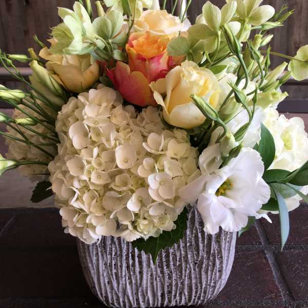 Mixed bouquet of cream and peach flowers in a ribbed white vase