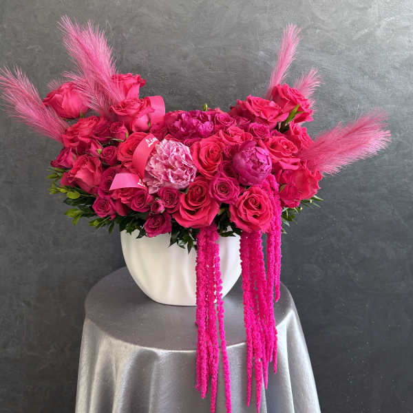 Hot pink rose arrangement in a white vase with pink feather accents