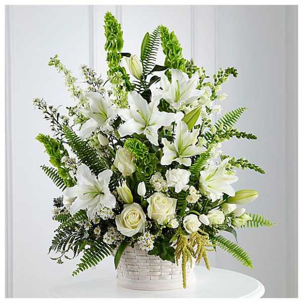 Tall arrangement of white lilies and roses with green Bells of Ireland in a white basket.