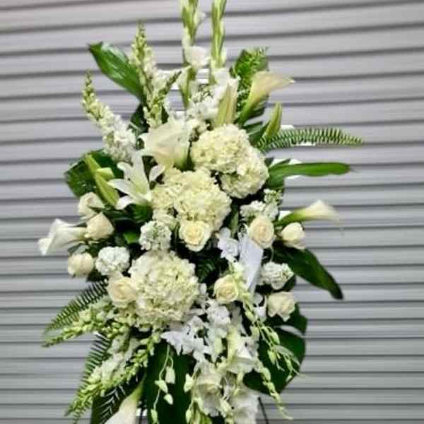 Tall white standing spray of mixed flowers and large tropical leaves on an easel.