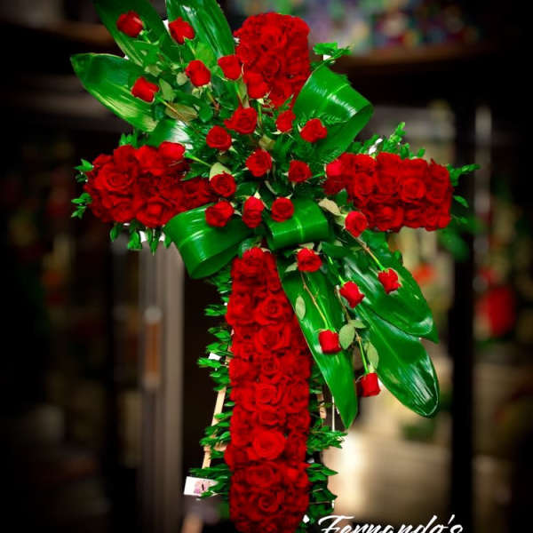 Tall standing cross of red roses with bold green leaves on an easel