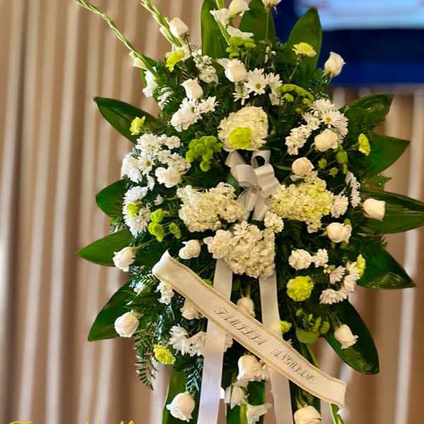 Tall standing spray of white and green flowers with ribbons on an easel