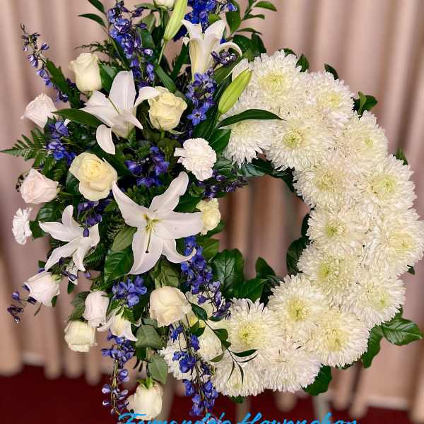 Standing white and blue sympathy wreath with lilies, roses, and mums on an easel