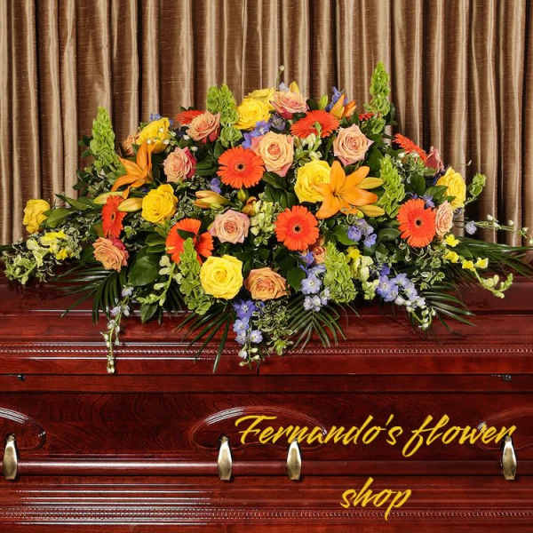 Bright orange and yellow casket spray with roses, gerbera daisies, and lilies on a wooden casket