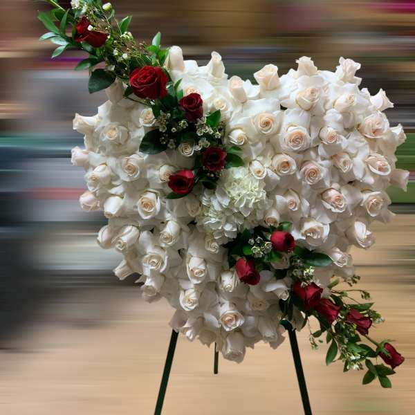 Heart-shaped standing spray of ivory roses with red roses accent on a metal easel.
