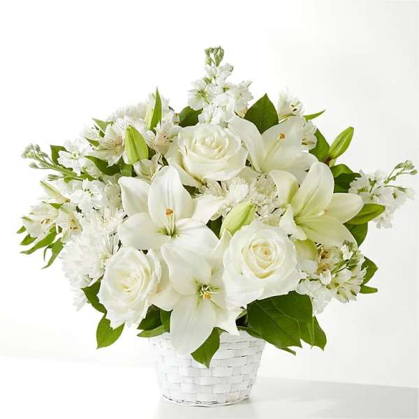 White lilies and roses arranged with other white blooms in a white woven basket